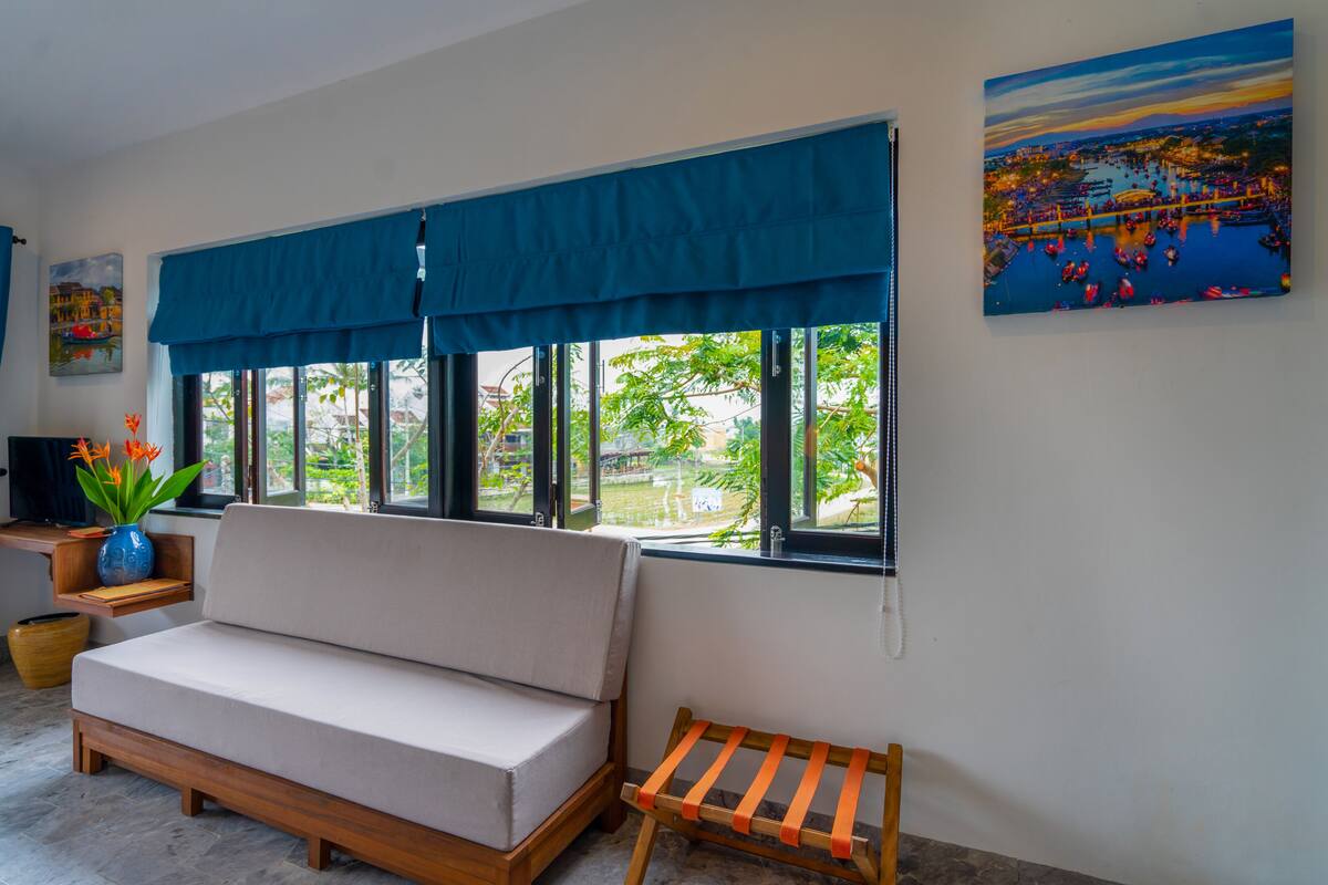 Une pièce comprenant un canapé, un petit banc en bois, un téléviseur posé sur un meuble, un vase avec des fleurs et un tableau accroché au mur.