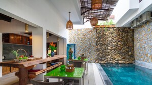 A poolside area with a stone wall, wooden furniture, and hanging lights. - Cat Tuong Boutique Villas (Da Nang)
