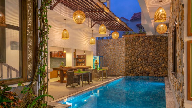 An indoor swimming pool with stone walls, wicker furniture, and hanging lights. - Cat Tuong Boutique Villas (Da Nang)