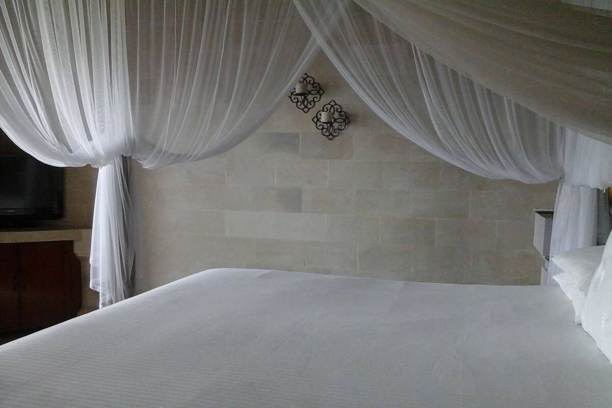 A bedroom with a bed, white curtains, and a stone wall.