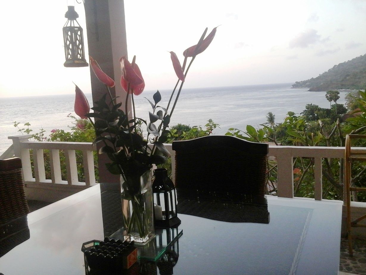 Una mesa con un jarrón de flores, un farol y vista al mar.