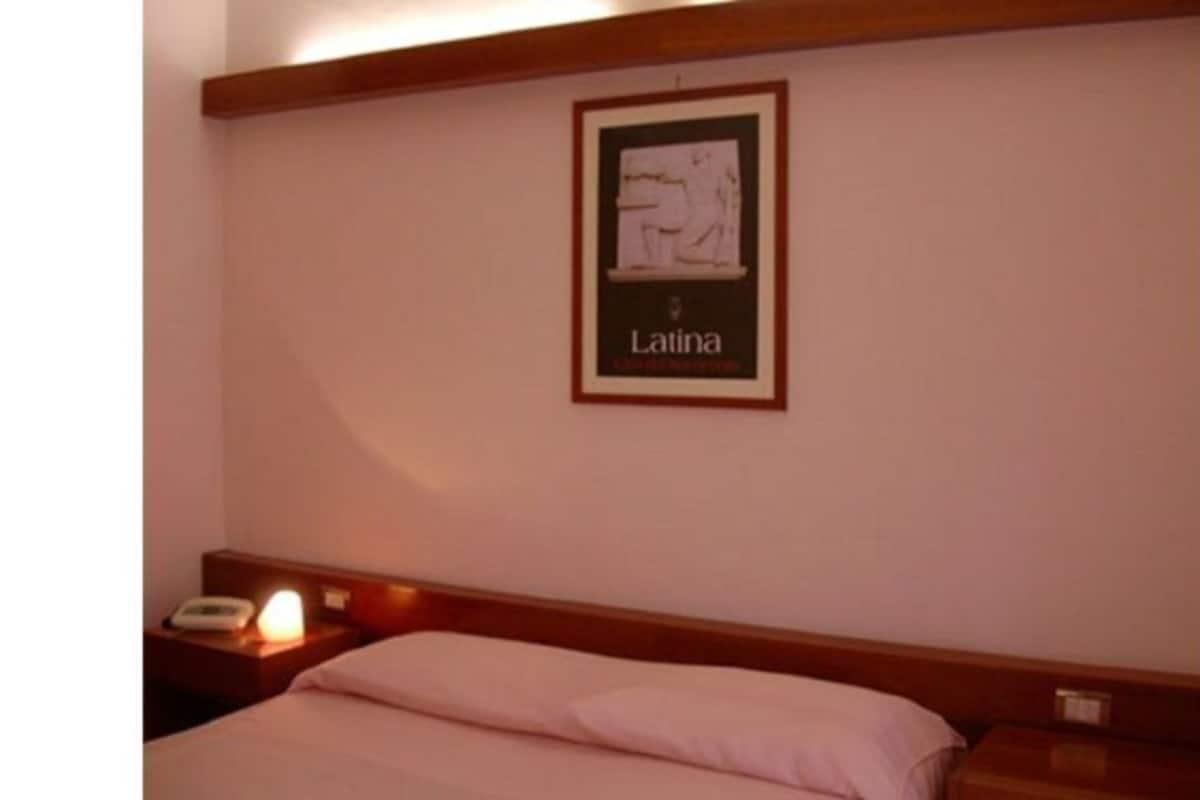 A hotel room with a bed, a nightstand, and a framed picture on the wall.