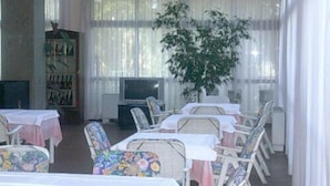 A dining area with tables and chairs, a television, and a large plant. - Hotel Excelsior (Latina)