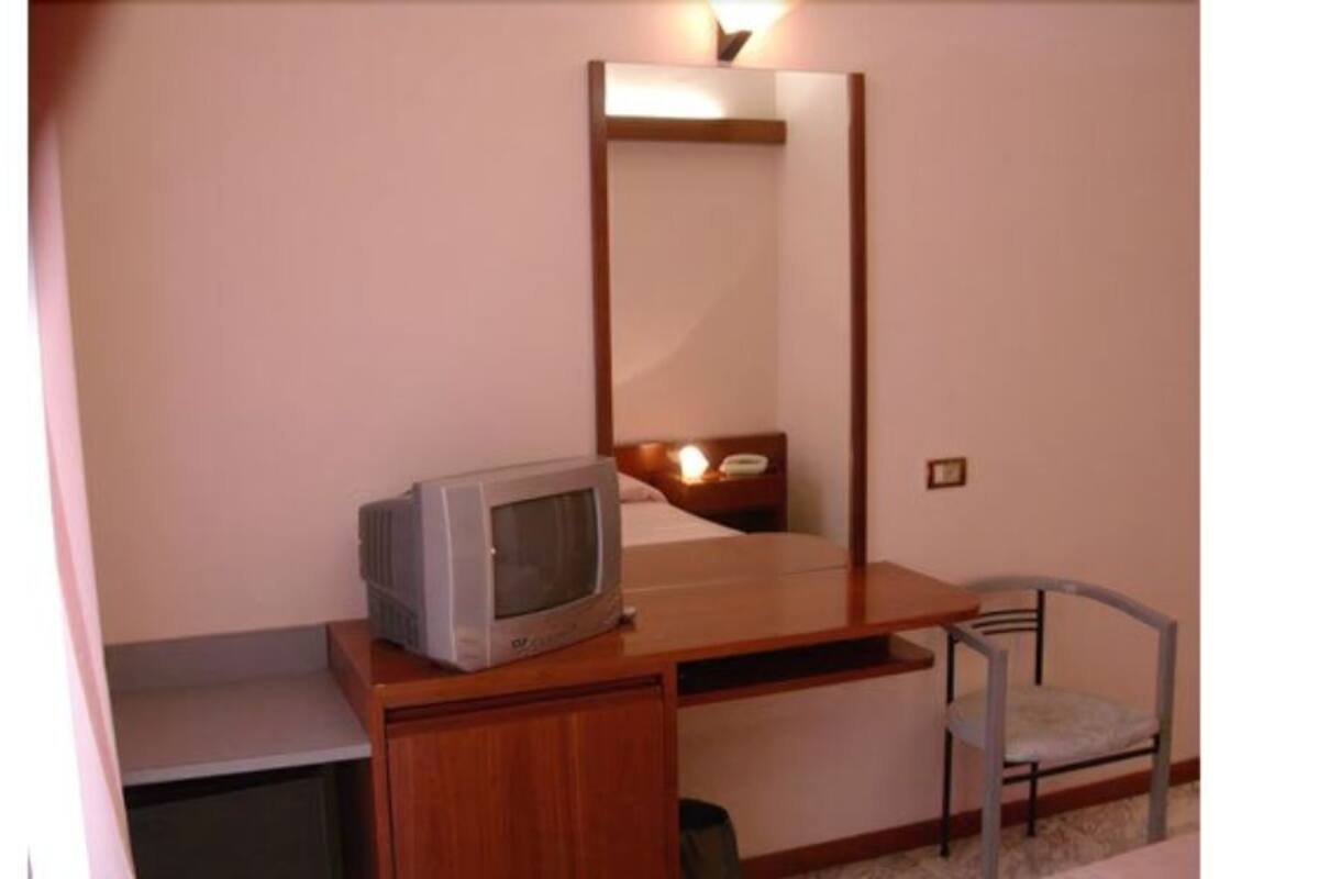 A small room with a wooden desk, a chair, a television, and a mirror.