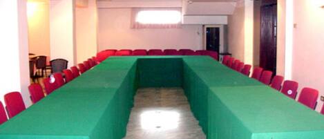 A conference room with a long table covered in green, surrounded by red chairs.
