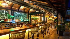 Una zona de bar con sillas de madera, una barra con botellas y plantas.