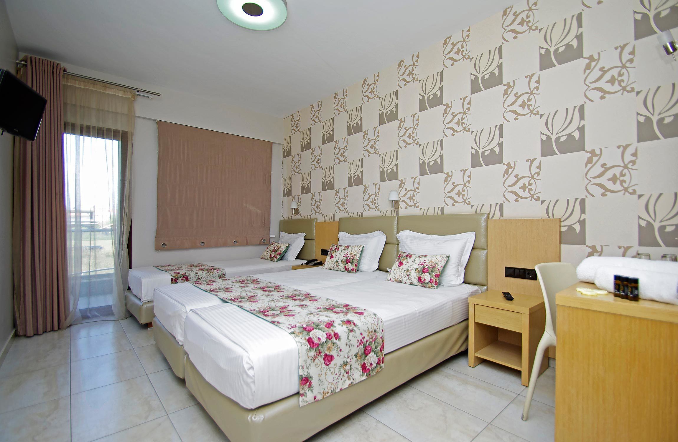 Habitación de hotel con dos camas, un escritorio, una silla, un televisor y una ventana con cortinas.