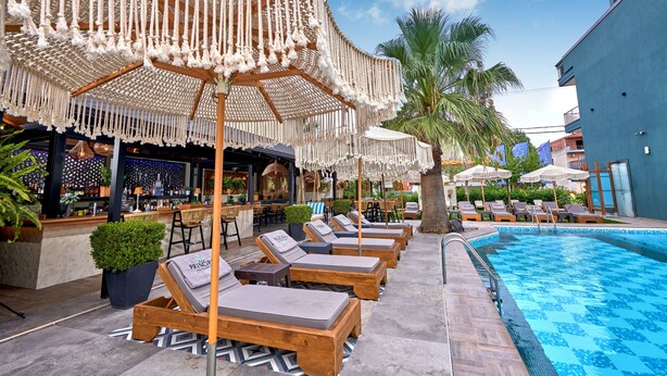 Zona de piscina con sillas de descanso y sombrillas, un bar y una piscina.