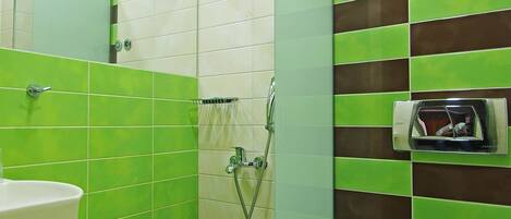 Een badkamer met groene en witte tegels, een douche, toilet en wastafel.