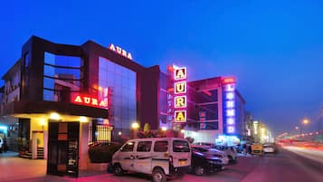 Un edificio con un llamativo letrero 'AURA', un estacionamiento y una calle con vehículos.