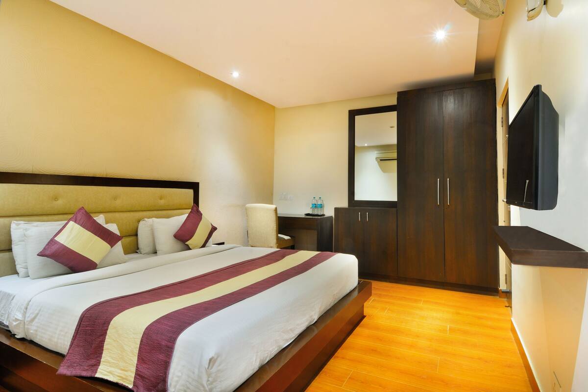 A hotel room with a large bed, a wardrobe, a flat-screen TV, and a bedside table with a lamp.