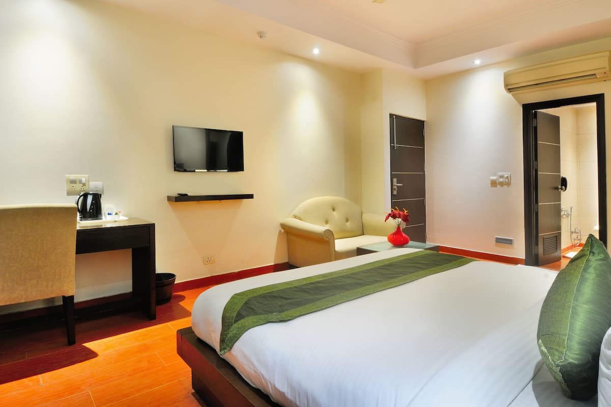 A hotel room with a bed, a desk, a chair, a TV, and a bathroom.