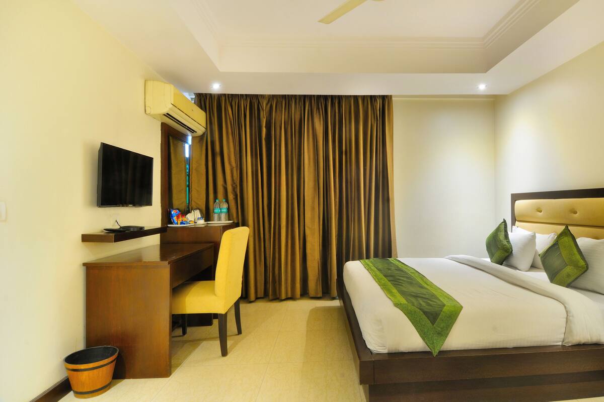 A hotel room with a bed, a desk, a chair, a television, and a curtain.