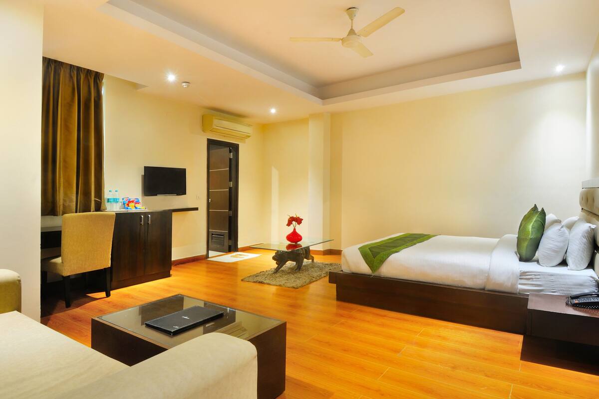A hotel room with a bed, a desk with a computer, a TV, and a ceiling fan.