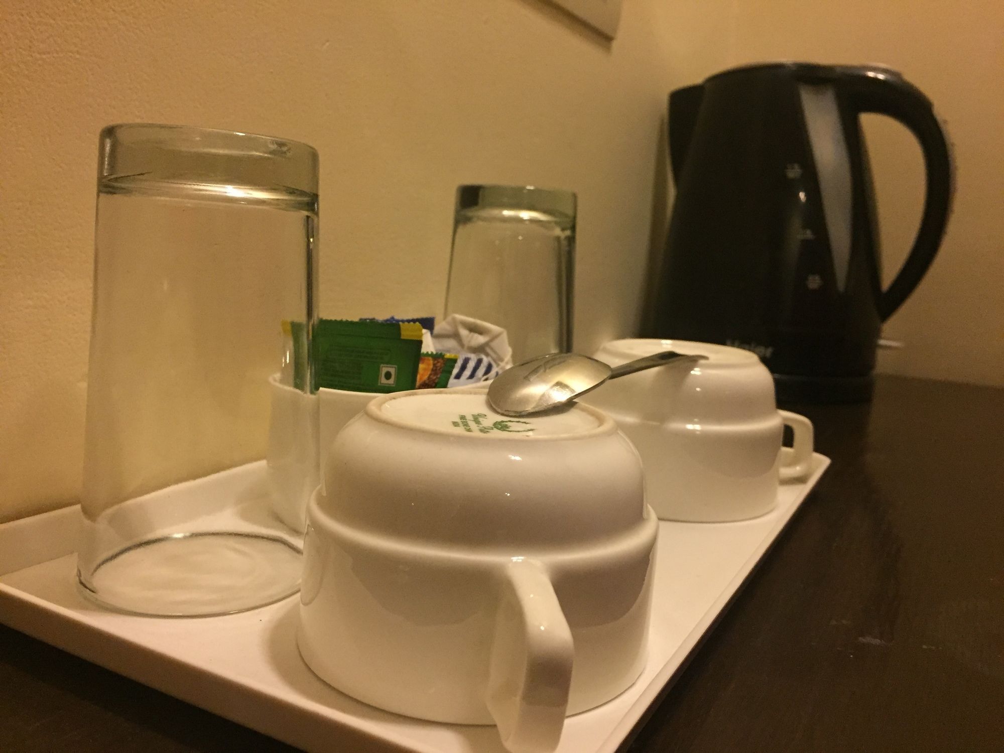 A tray with two white cups, one with a spoon, and two clear glasses on a table.