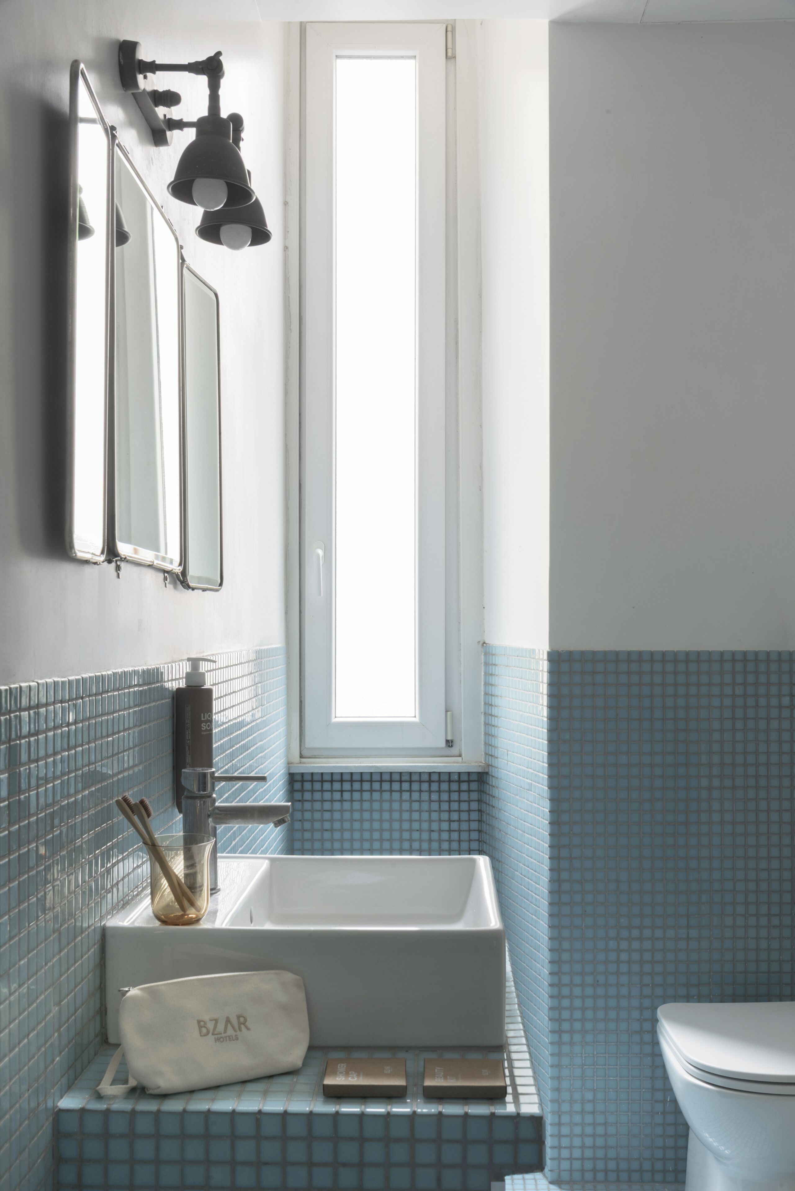 A bathroom with a white sink, a mirror, a window, and a toilet.