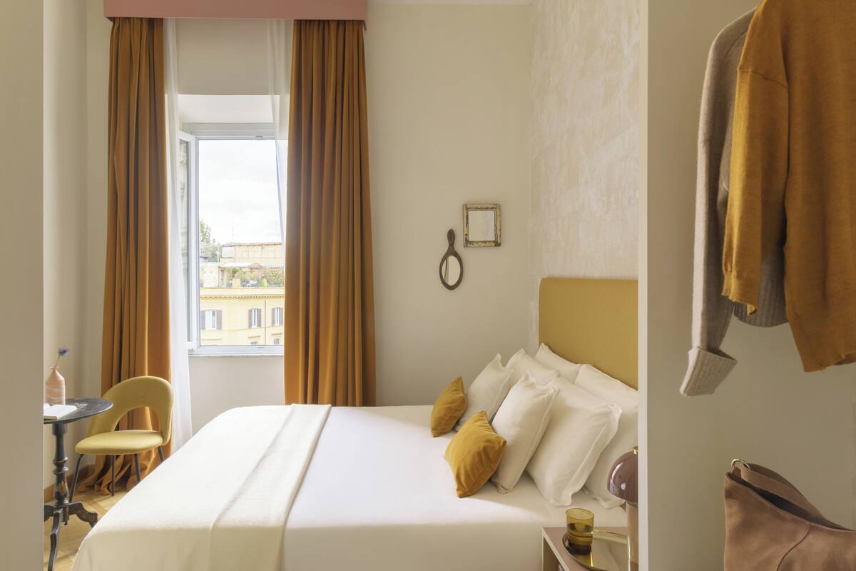 Ein Hotelzimmer mit Bett, Sessel, Tisch und einem Vorhangfenster.