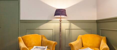 Two yellow armchairs with newspapers, a tall floor lamp, and a green wall with paneling.