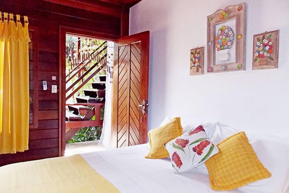 Une chambre à coucher avec un lit, des rideaux jaunes, une porte en bois et un escalier menant à l’extérieur.