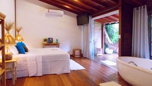 A bedroom with a bed, bedside table, lamp, and a view of the outside. - Pousada Riacho dos Cambucás (Angra dos Reis)