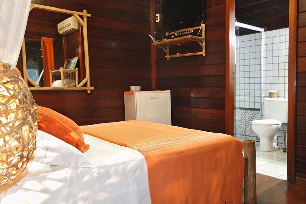 Une chambre dans un chalet en bois, comprenant un lit, un petit réfrigérateur, un miroir et une salle de bain avec des toilettes et un lavabo.