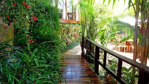 A wooden pathway leading through a lush garden with various plants and a wooden railing. - Pousada Riacho dos Cambucás (Angra dos Reis)