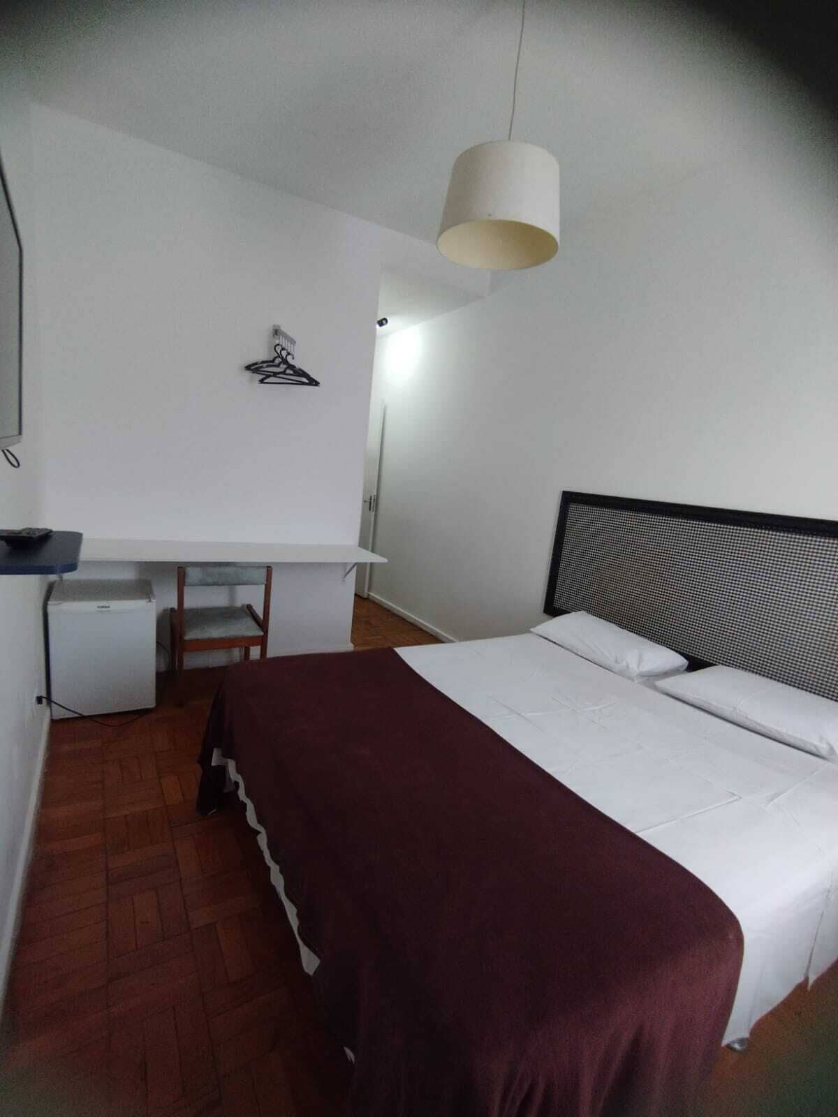 Un dormitorio con cama, escritorio, silla y lámpara colgante.