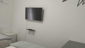 Quarto com cama, mesinha de cabeceira, televisão na parede e um varal de roupas.