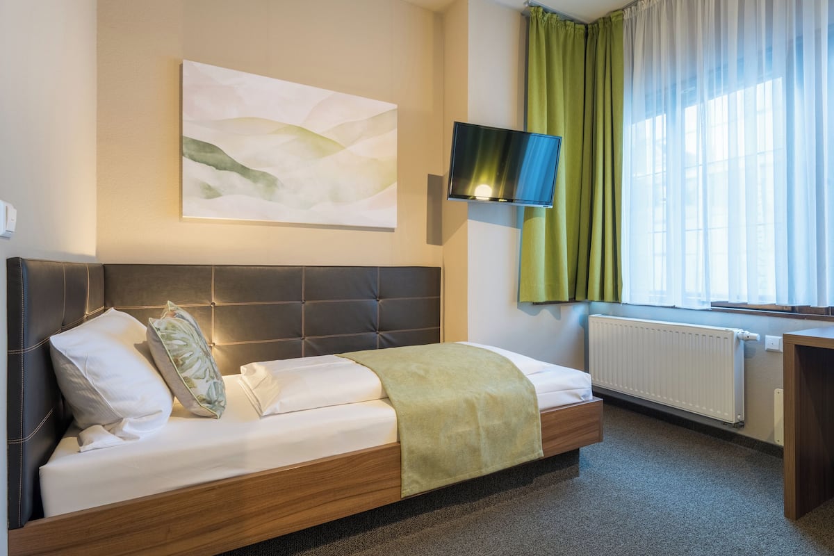 Een moderne hotelkamer met een bed, een flatscreen televisie, een radiator en een raam met gordijnen.
