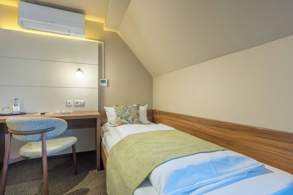 Een kamer met een bed, een bureau, een stoel, een airconditioner en een wandlamp.