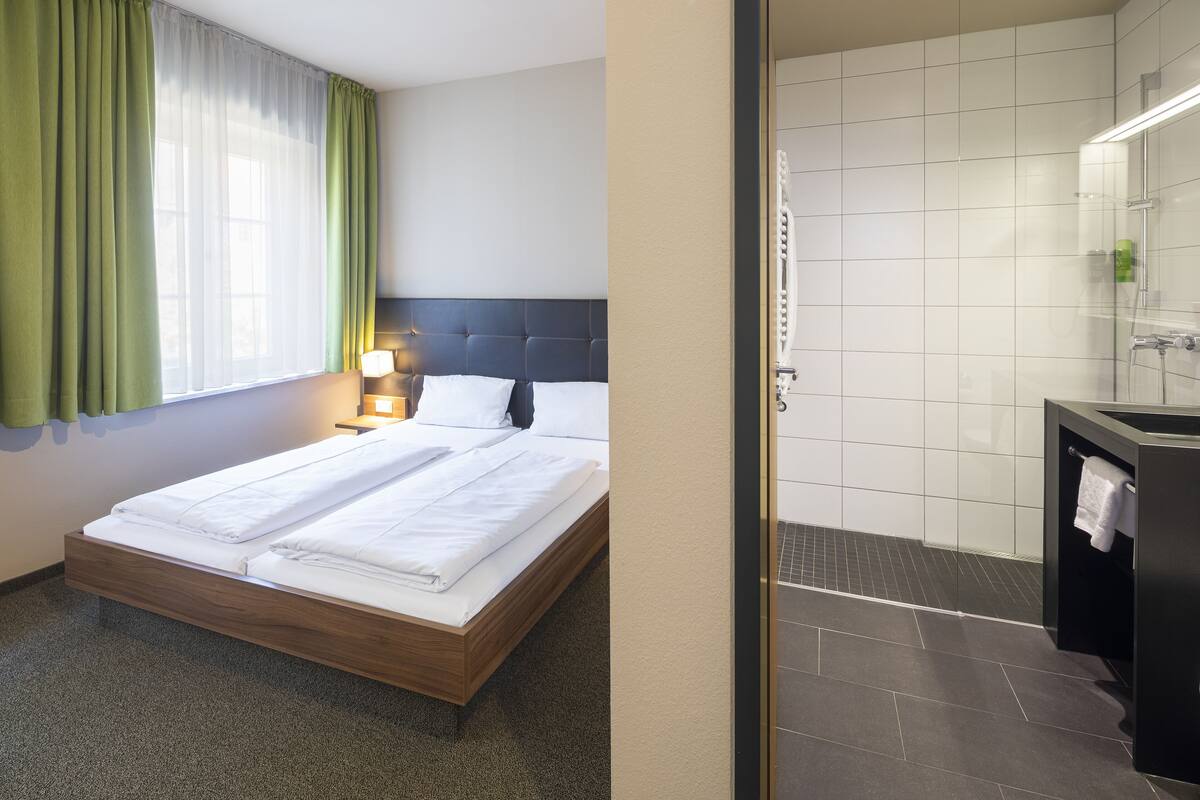 Een hotelkamer met een bed, een bedlamp, een badkamer met douche en een wastafel.