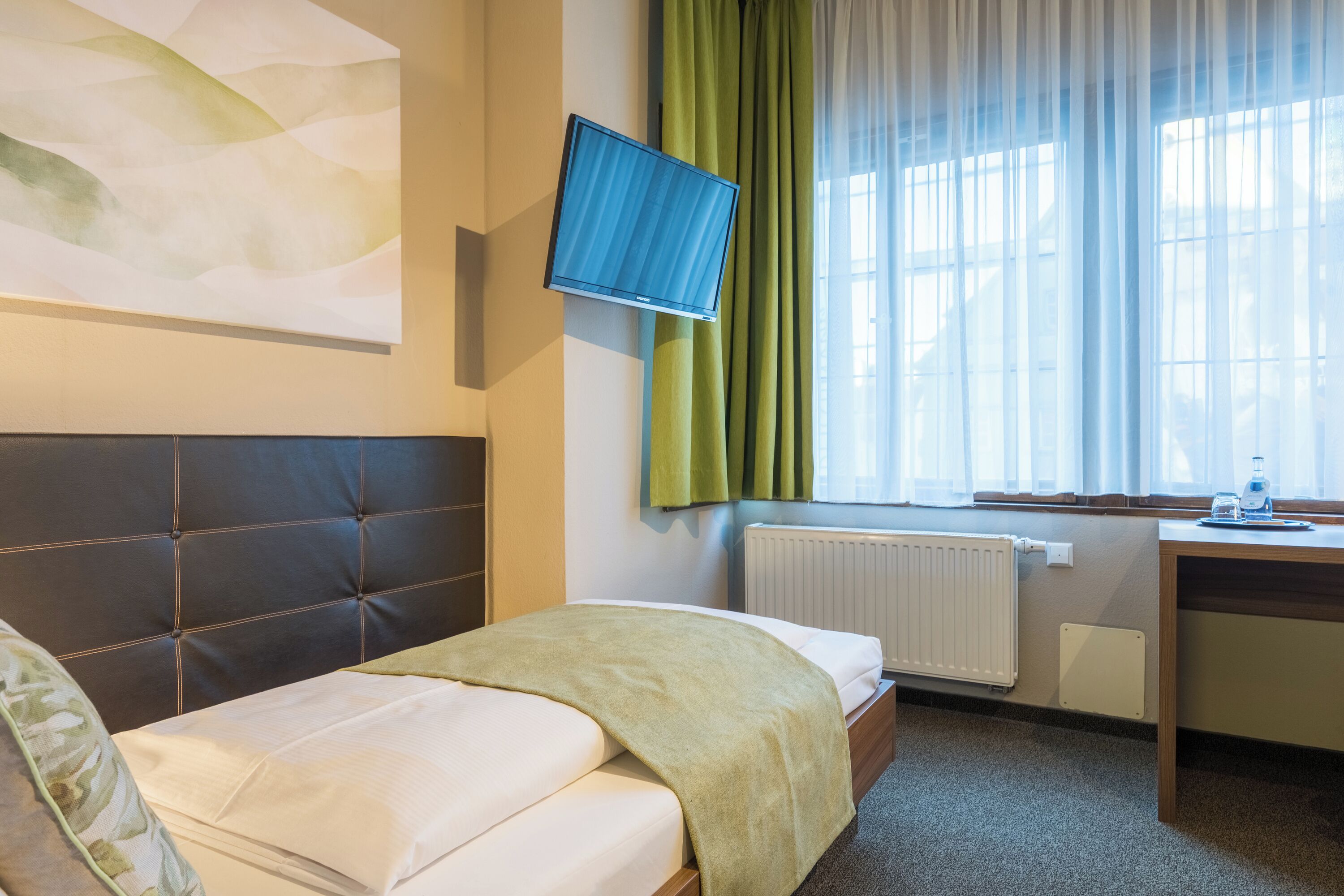 Ein Hotelzimmer mit einem Bett, einem Schreibtisch, einem Fernseher und einem Fenster mit Vorhängen.