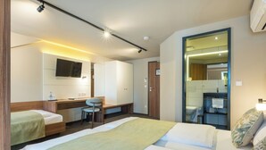 A hotel room with a bed, a desk, a chair, a television, a mirror, and a bathroom visible through an open door.