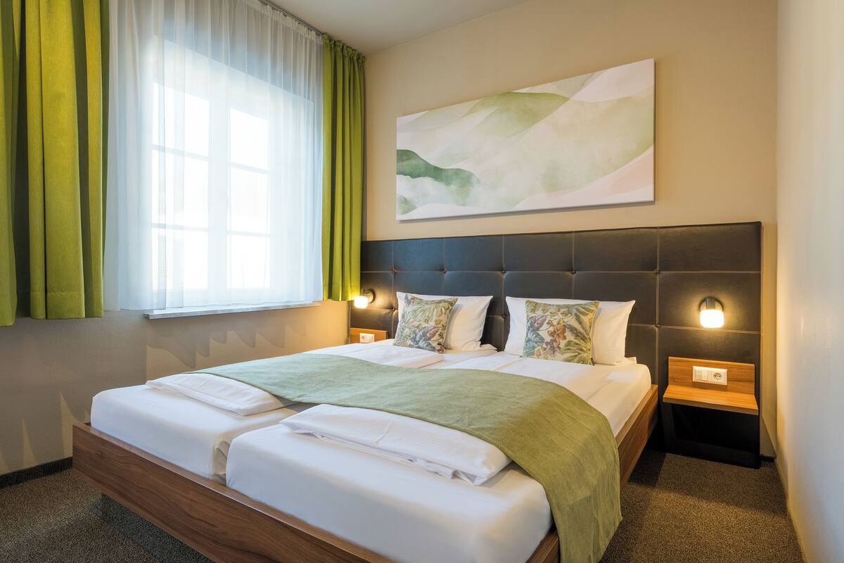 Een hotelkamer met een groot bed, een nachtkastje, een wandlamp en een raam met gordijnen.