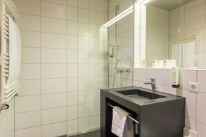 Une salle de bain avec des murs recouverts de carreaux blancs, une douche en verre, un lavabo avec un porte-serviettes et un miroir.