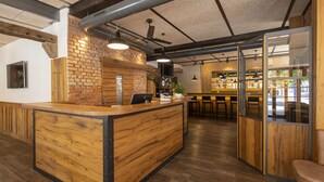 A reception area with a wooden counter, a brick wall, and a bar area in the background.