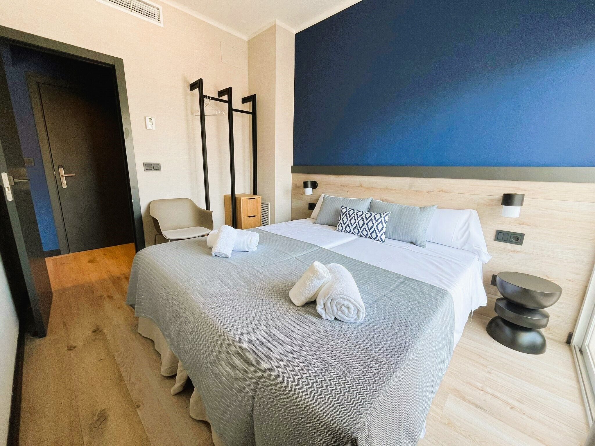 Quarto de hotel com uma cama grande, uma cadeira, um porta-roupas e uma parede azul.