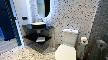 Un baño moderno con un lavabo redondo, inodoro y zona de ducha.