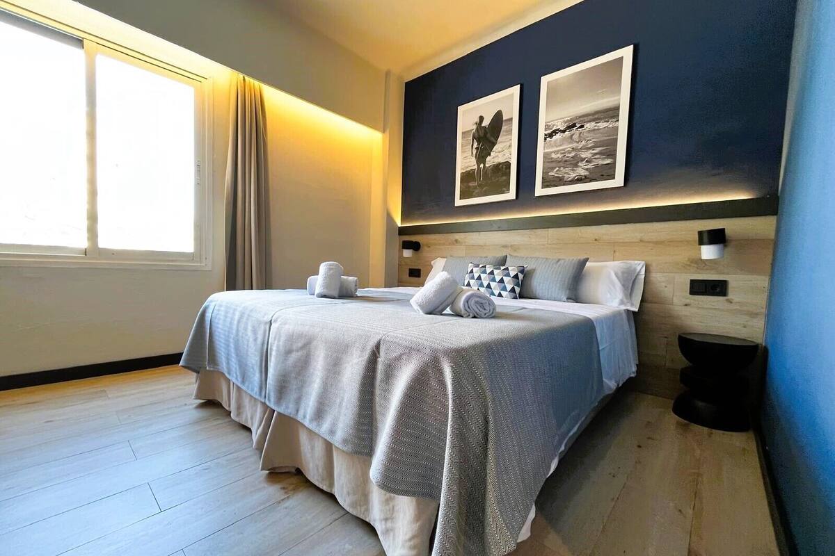 Une chambre moderne avec un grand lit, deux lampes fixées au mur et deux tableaux encadrés.