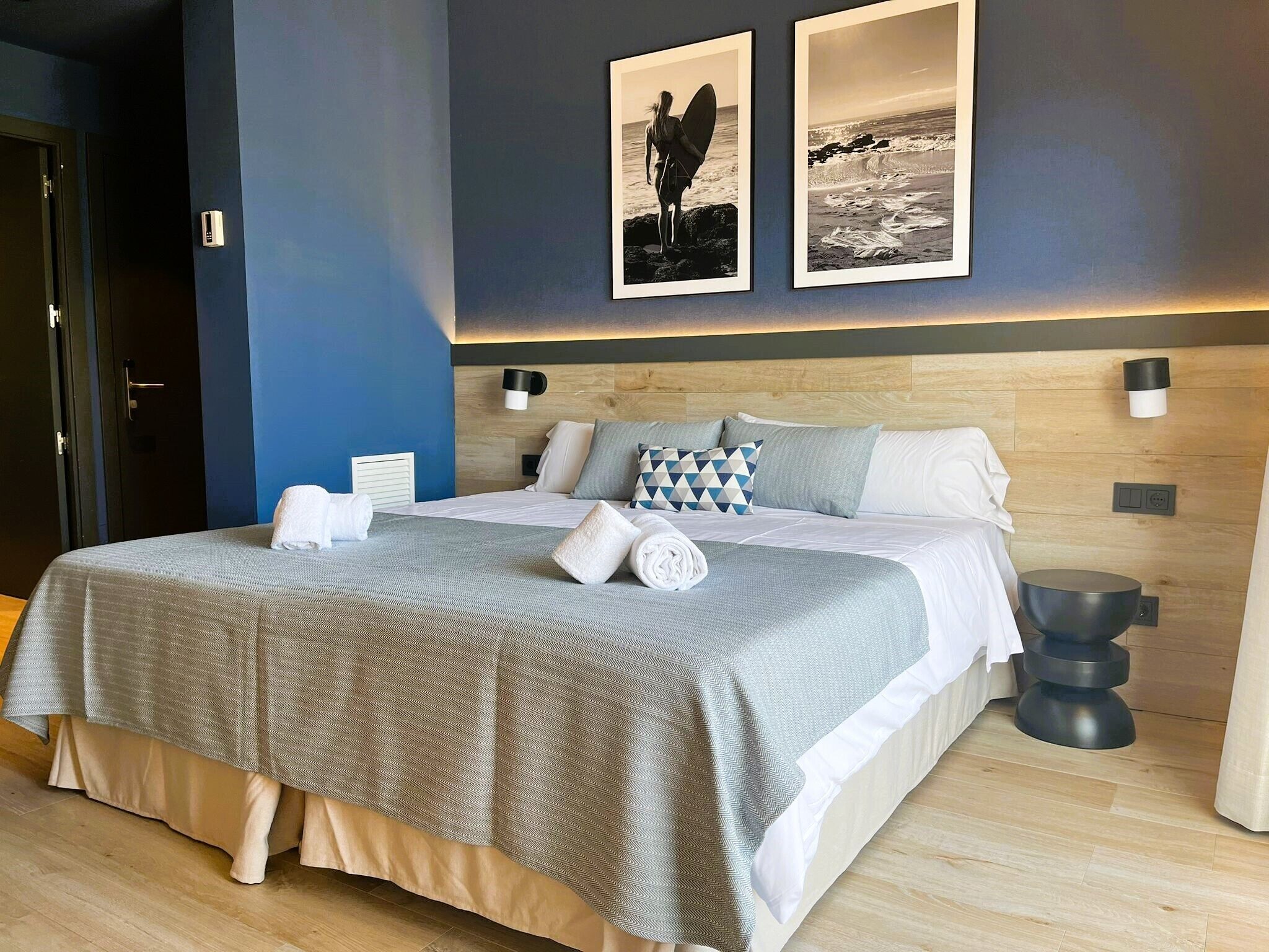 A modern hotel room with a large bed, a wooden headboard, and two framed pictures on the wall.