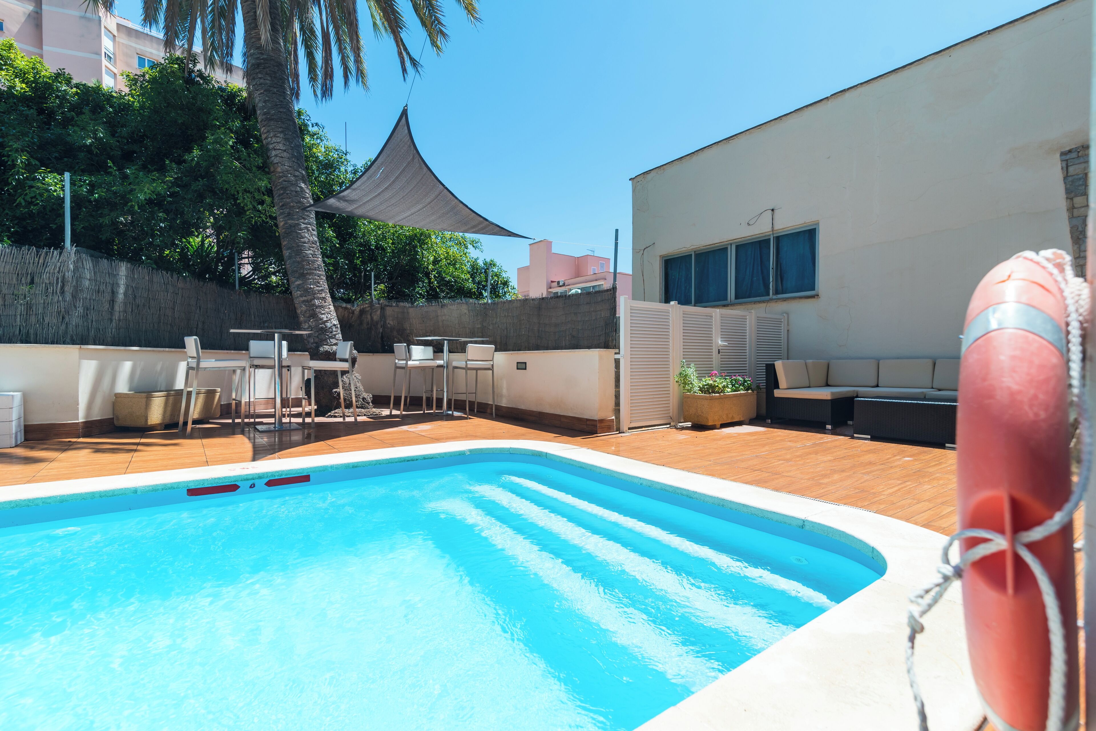 Une piscine équipée d’une bouée de sauvetage, avec des sièges à l’extérieur et un palmier.