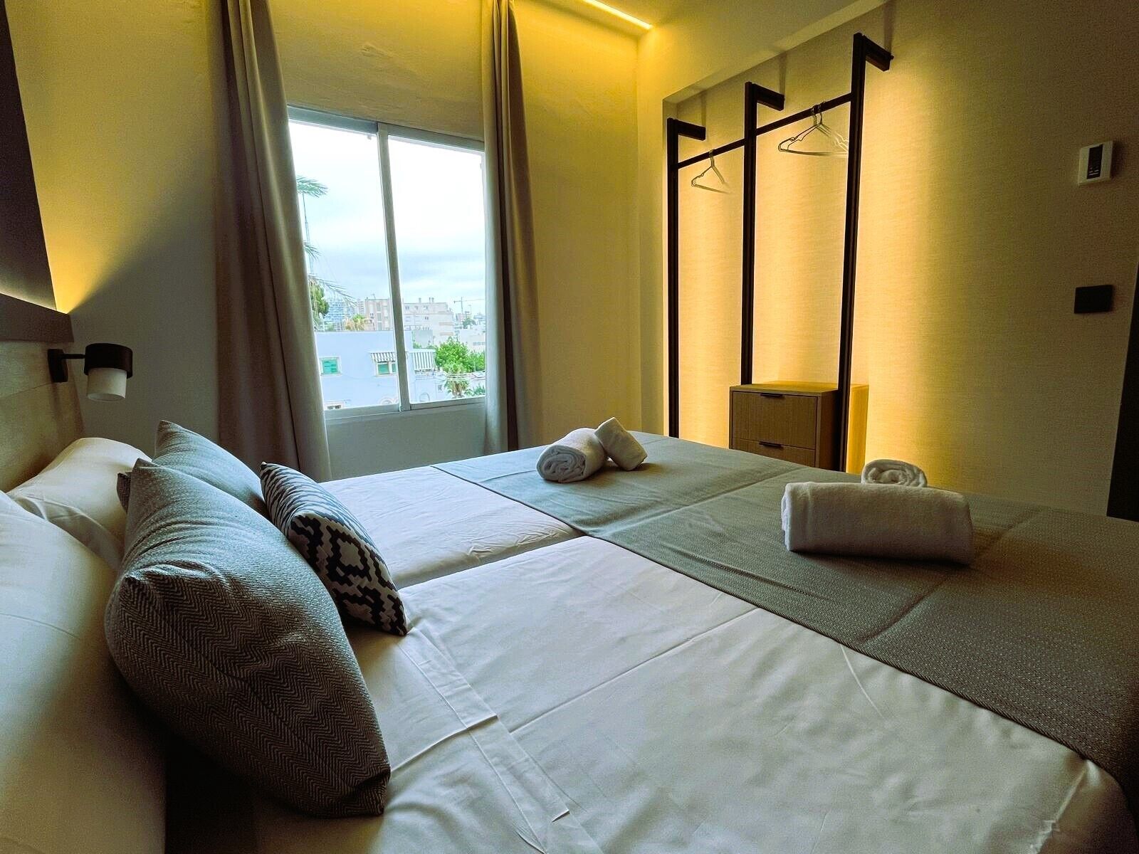 Une chambre d’hôtel avec deux lits, une fenêtre donnant sur un paysage agréable, une table de chevet et un porte-manteau mural.
