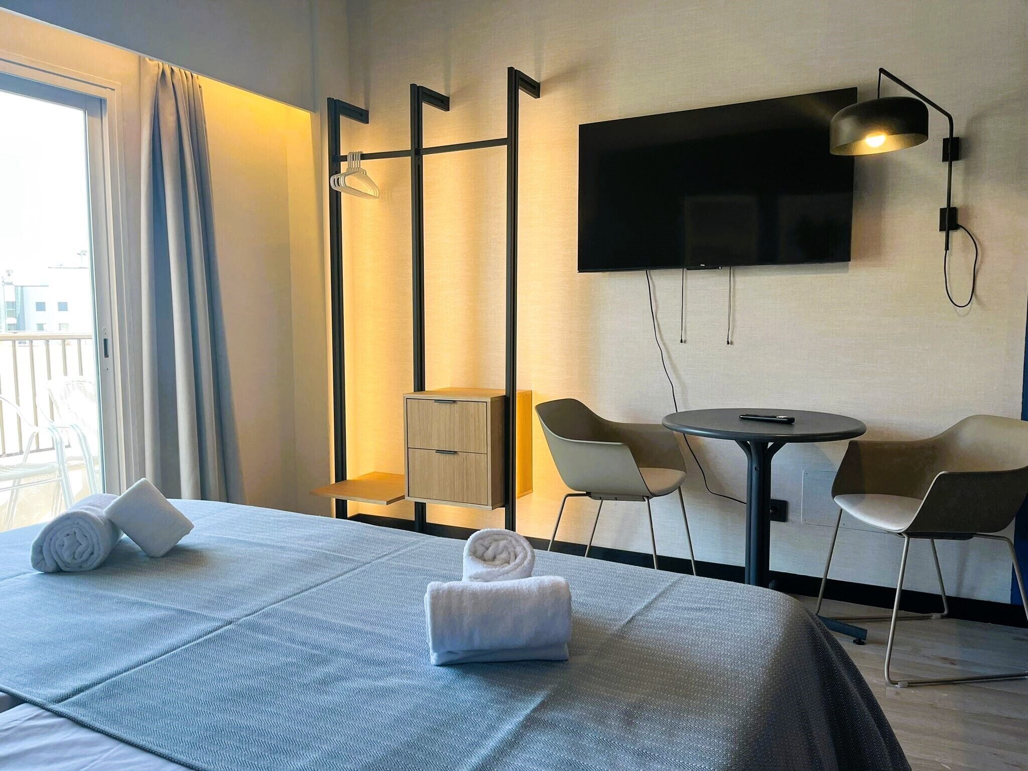 Habitación de hotel con cama, escritorio, dos sillas, televisor y ventana con cortinas.