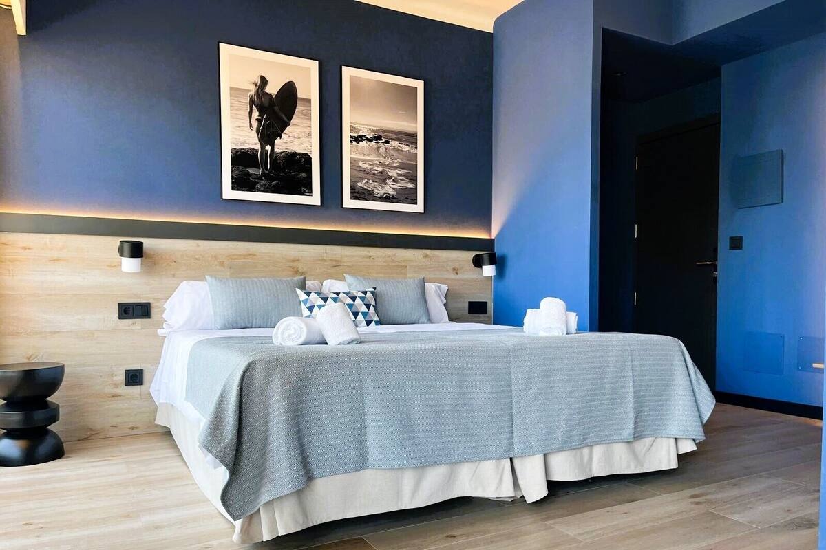 Une chambre à coucher moderne avec un grand lit, une tête de lit en bois et deux photographies encadrées accrochées au mur.