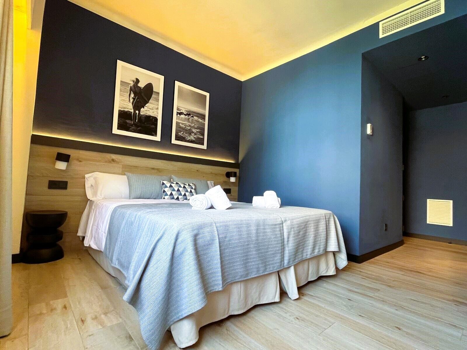 A modern bedroom with a bed, pillows, and a headboard. There are two framed pictures on the wall.