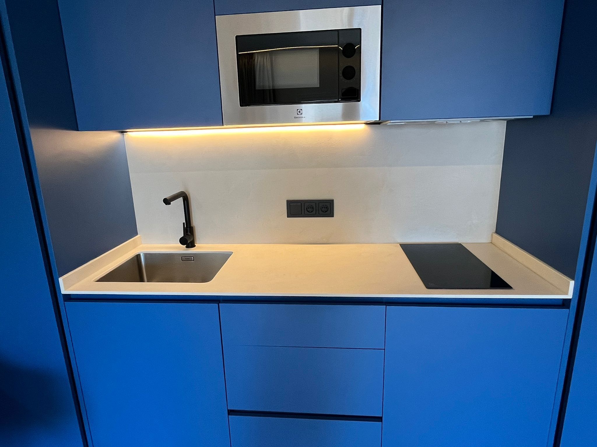 Una kitchenette compacta con microondas integrado, un lavamanos y un enchufe.