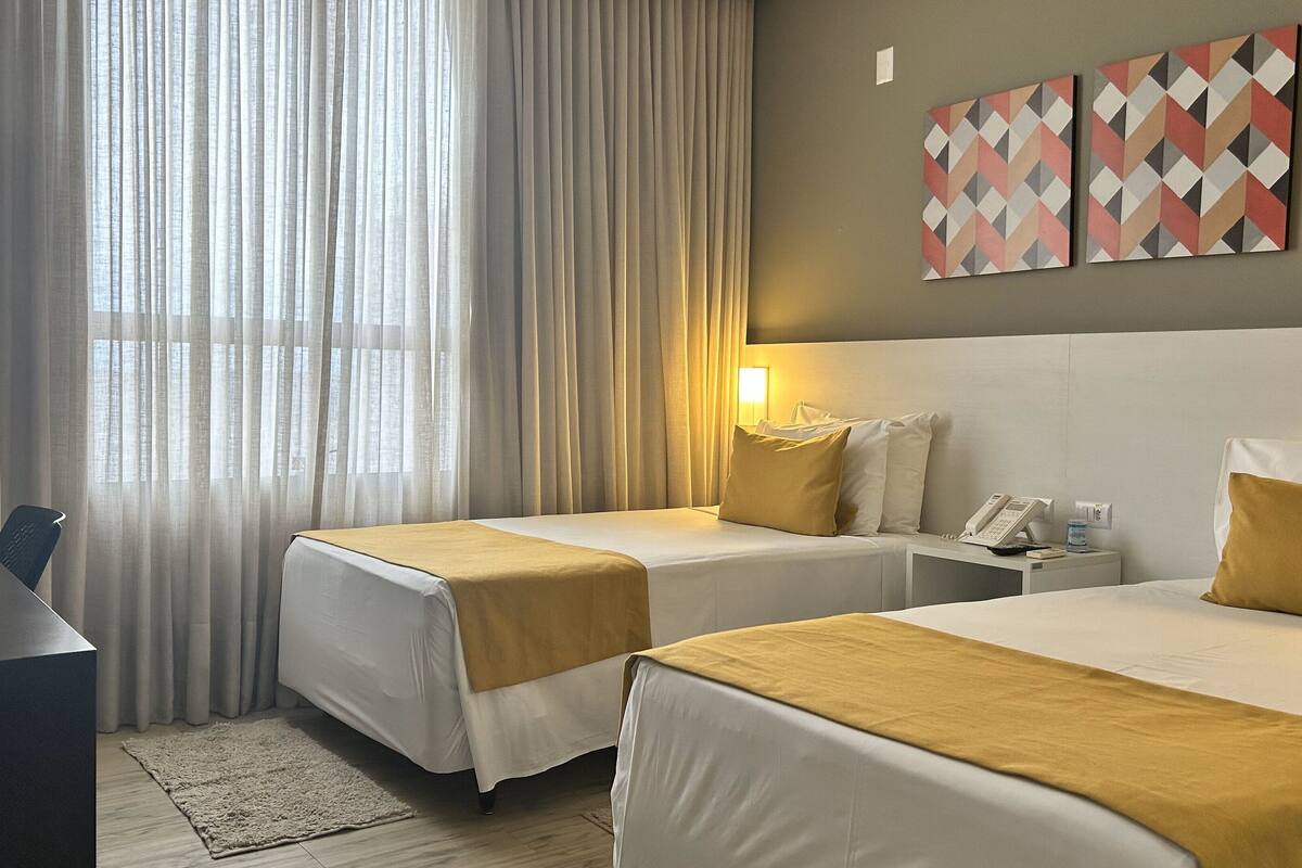 A hotel room with two beds, a desk, a telephone, and a wall-mounted artwork.