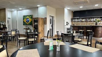 A restaurant with round tables and chairs, a bar area with bottles, and a painting on the wall.