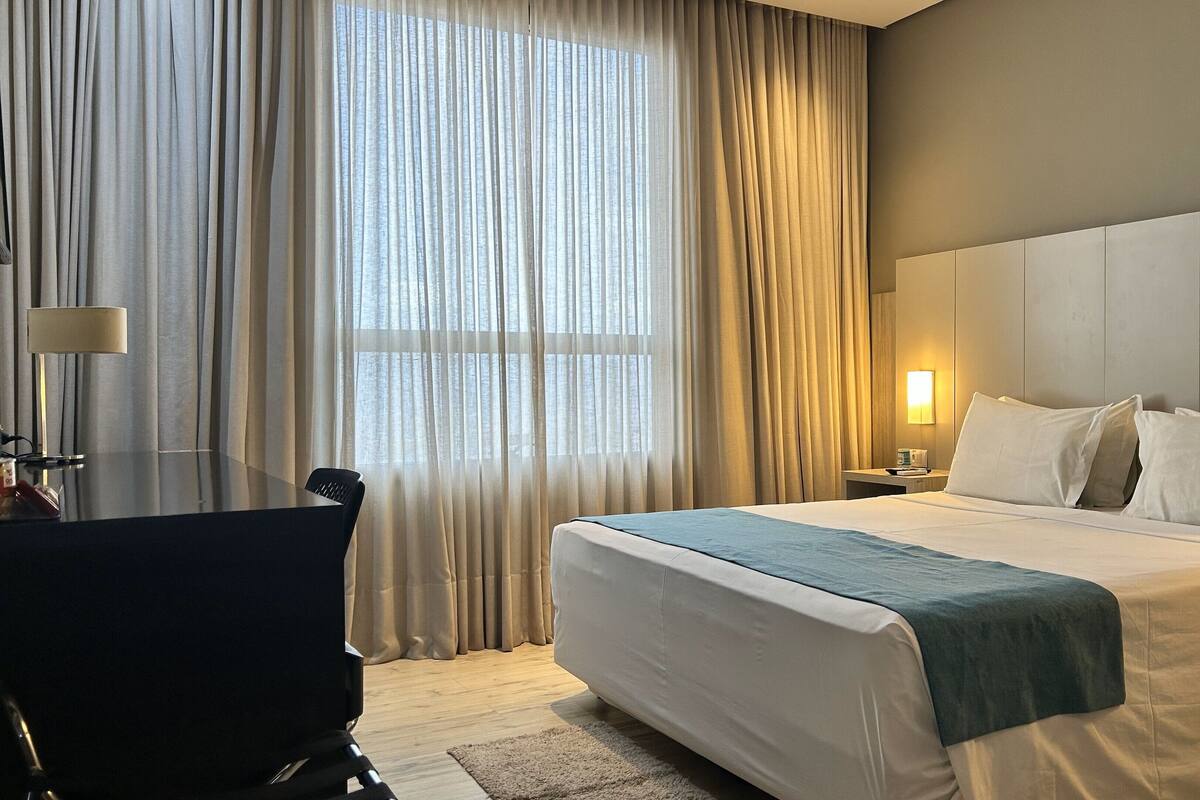 A hotel room with a large bed, a desk, and a chair.