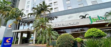 Un hotel con fachada moderna, un letrero Comfort Hotel & Suites, el restaurante Jambu Essence y exuberante jardinería.